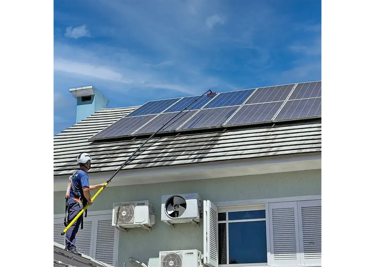 Un technicien utilise une perche télescopique pour nettoyer des panneaux solaires sur un toit.