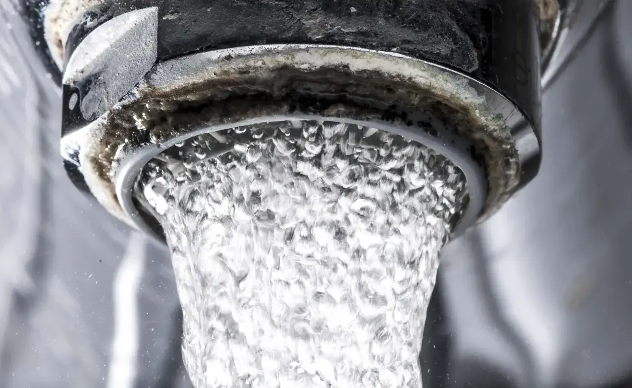 Agua fluyendo de un grifo con acumulaci&oacute;n de cal en las tuber&iacute;as.