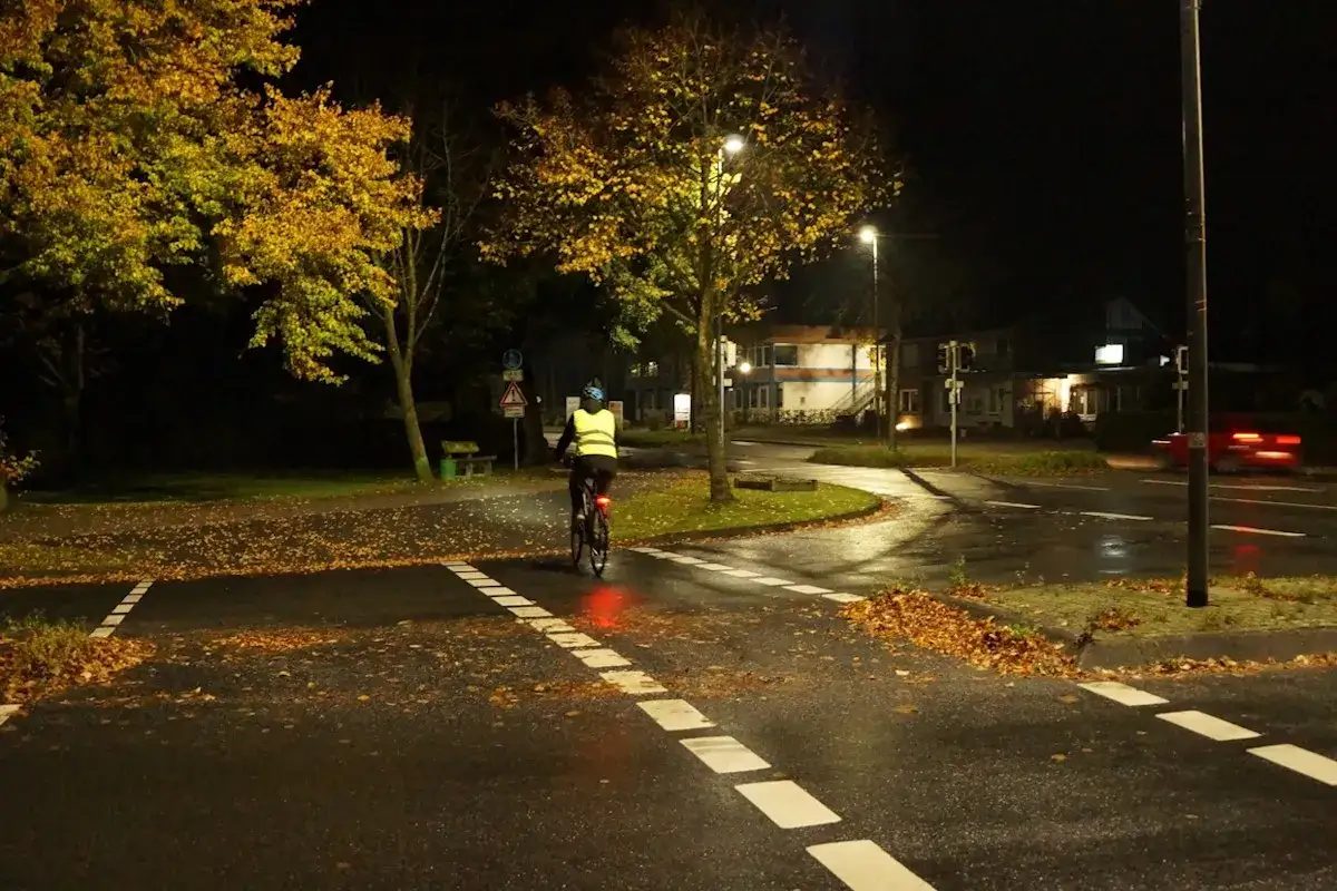 Radfahrer mit warnweste fahrrad verboten? Nein, er ist sichtbar und sicher unterwegs. Herbstlaub auf nasser Stra&szlig;e bei Nacht.
