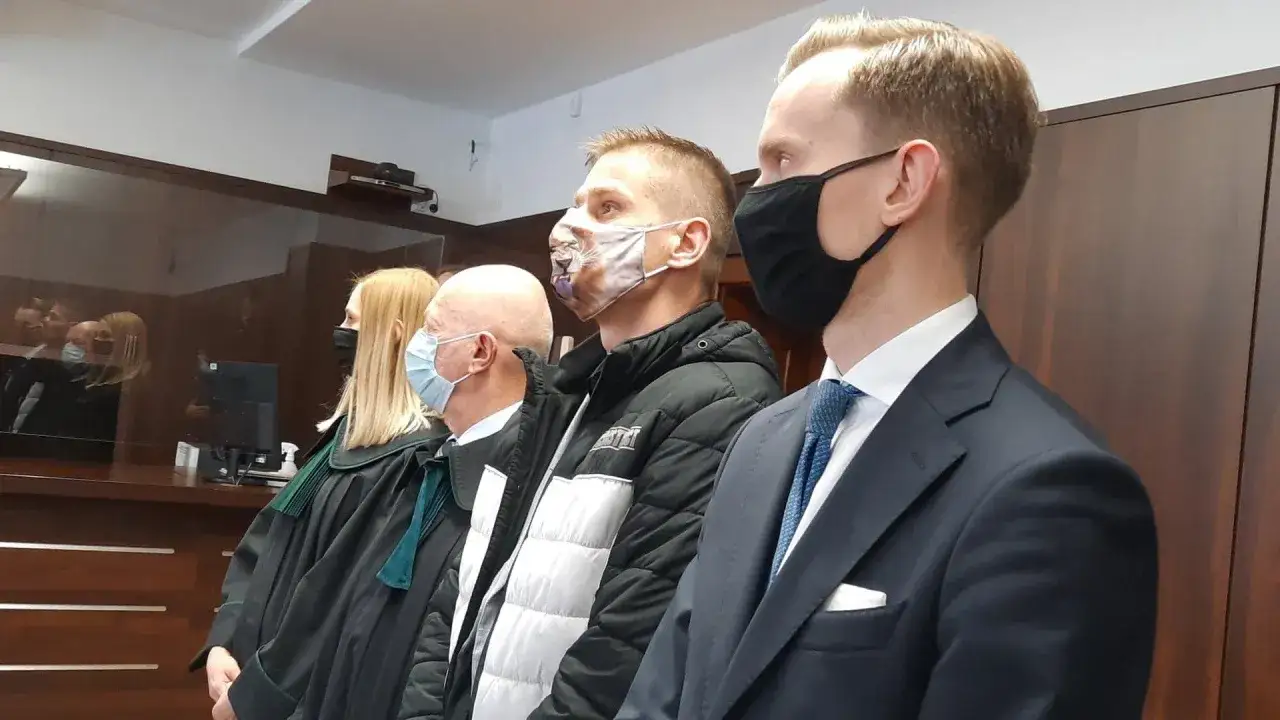 Tomasz Komenda w sądzie, w masce z lwem, czeka na odszkodowanie. Obok prawnicy w togach i garniturze.