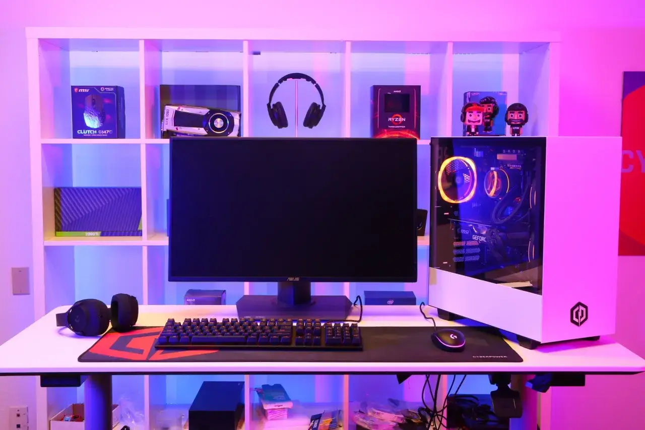 Stacja gamingowa z PC i monitorem, porównanie ps5 vs pc. Na półkach podzespoły komputerowe i gadżety.
