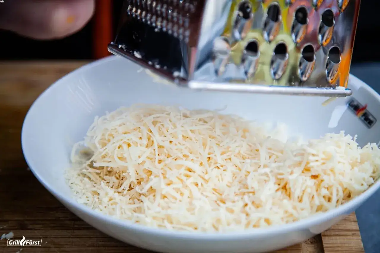 Parmesan wird gerieben, um ihn für das parmesan einfrieren vorzubereiten. Feine Käsestücke landen in einer weißen Schüssel.