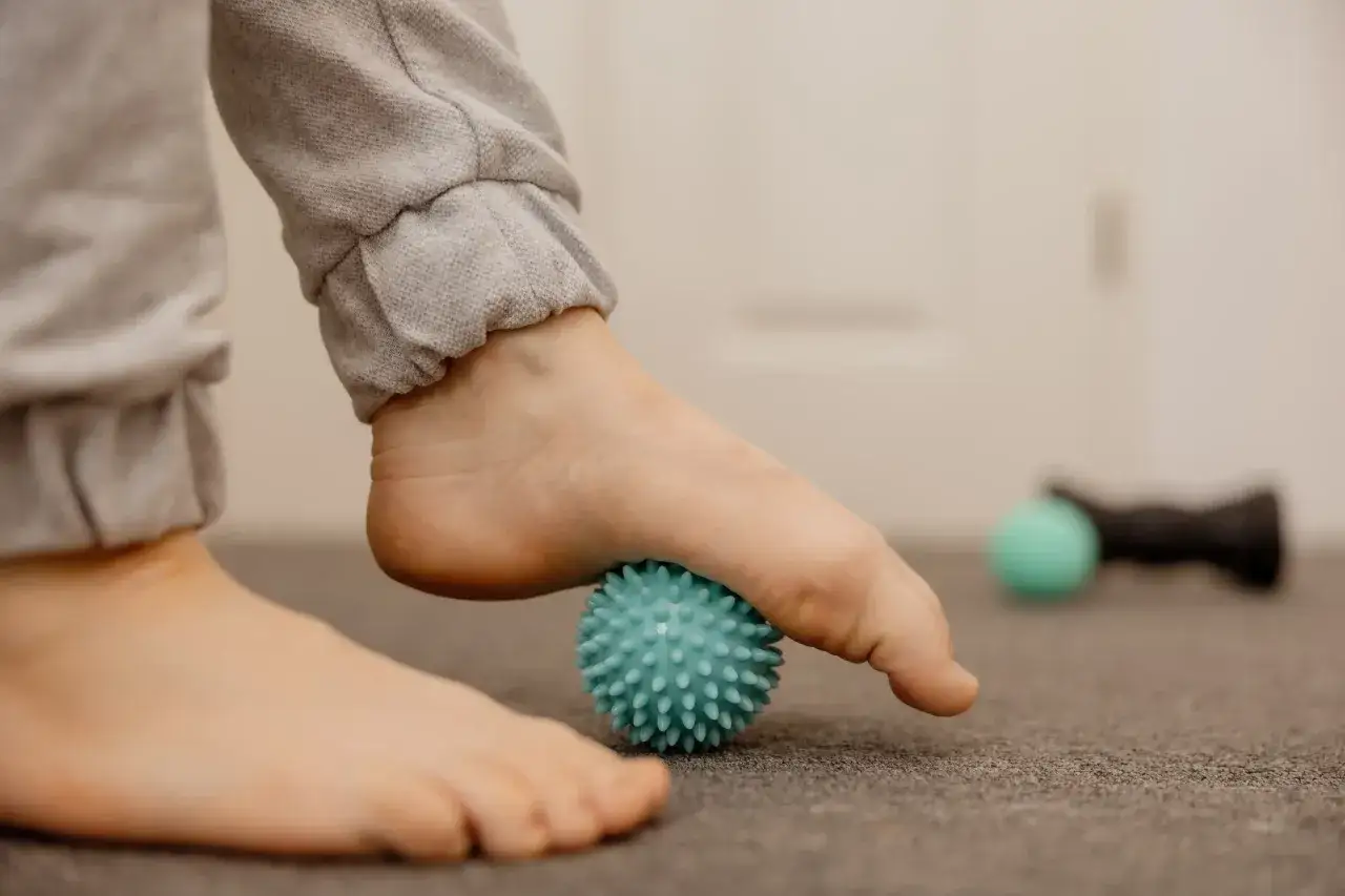 A person's foot rolls on a spiky blue ball, a simple yet effective aching feet remedy.