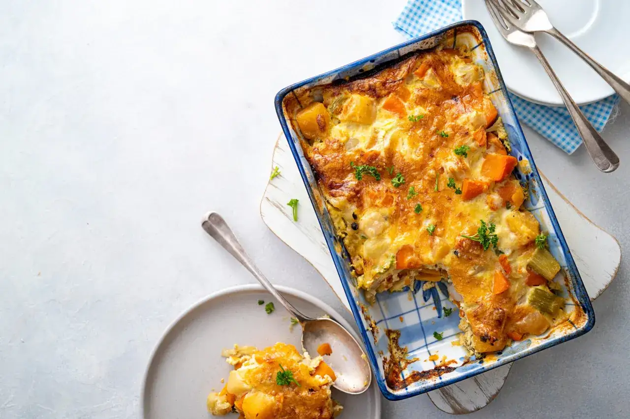 Un gratin de courge aux l&eacute;gumes, dor&eacute; et app&eacute;tissant, servi dans un plat bleu et blanc. Une portion est d&eacute;j&agrave; servie dans une assiette.