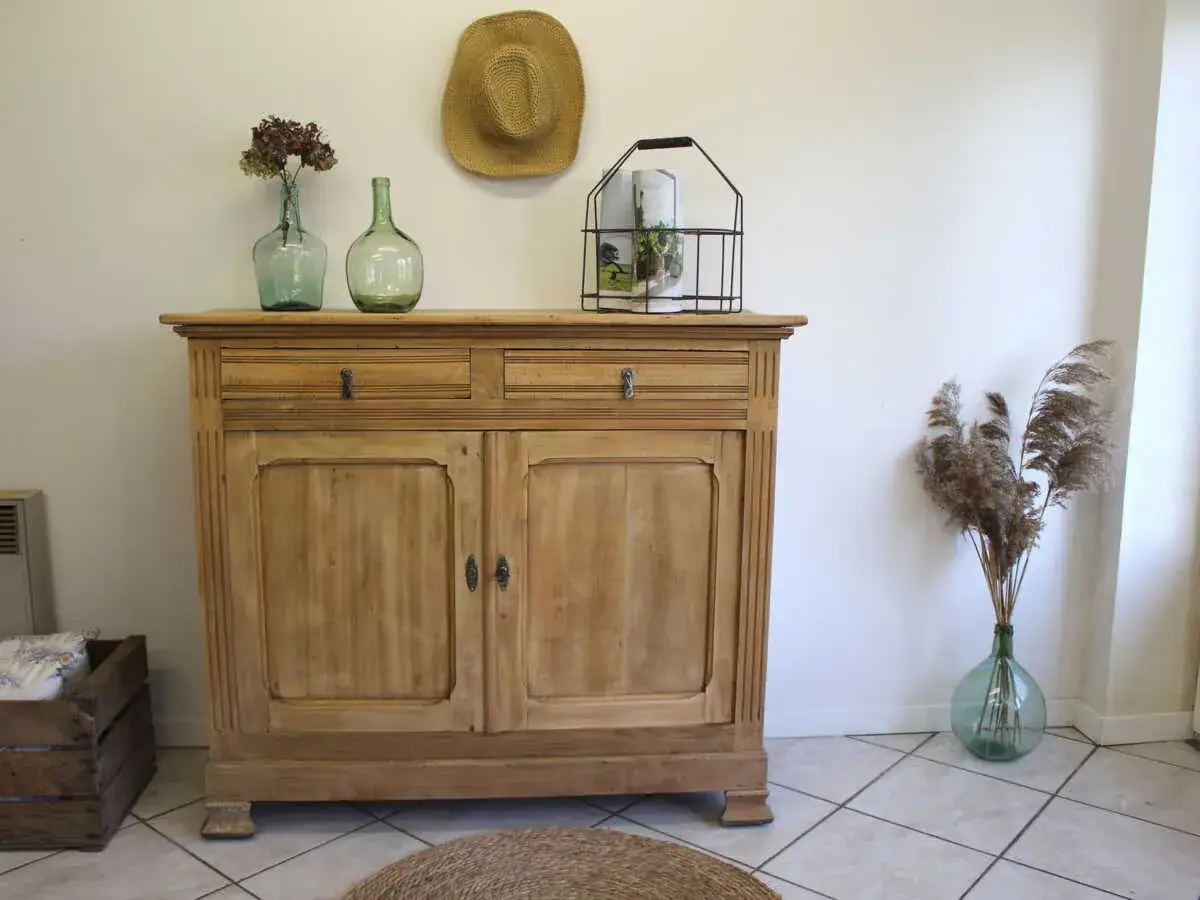 Un meuble ancien en bois clair, patiné par le temps, avec deux portes et deux tiroirs. Une touche vintage pour votre intérieur.
