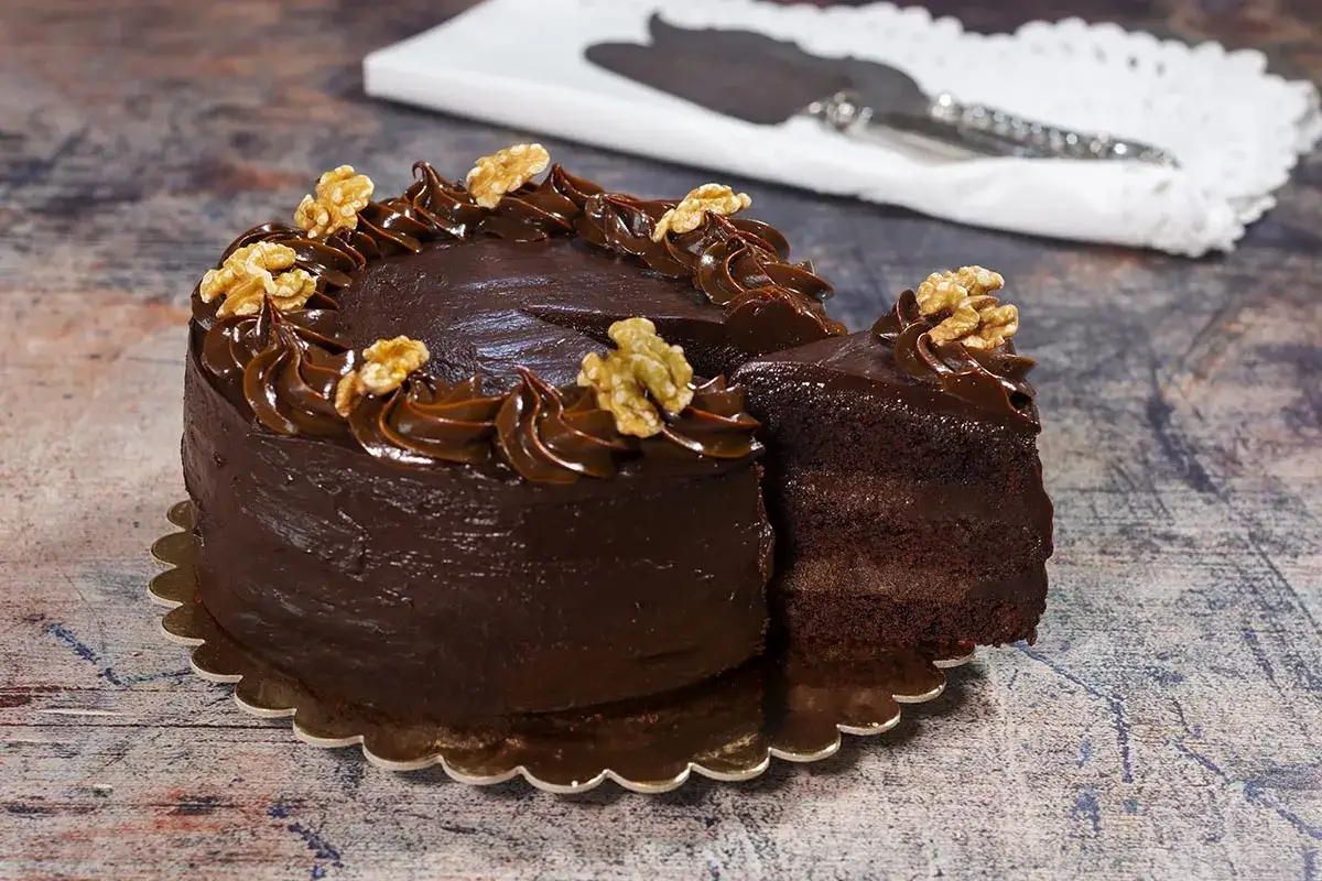 Tarta de chocolate con cobertura cremosa y nueces. Una porci&oacute;n ya cortada revela sus capas esponjosas.