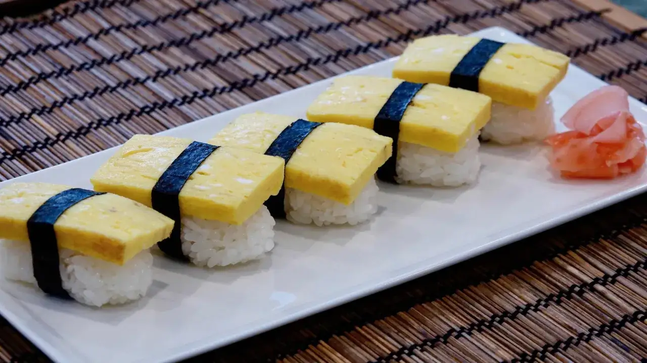 Sześć kawałków sushi z ryżem, nori i żółtym omletem do sushi. Obok różowy imbir.