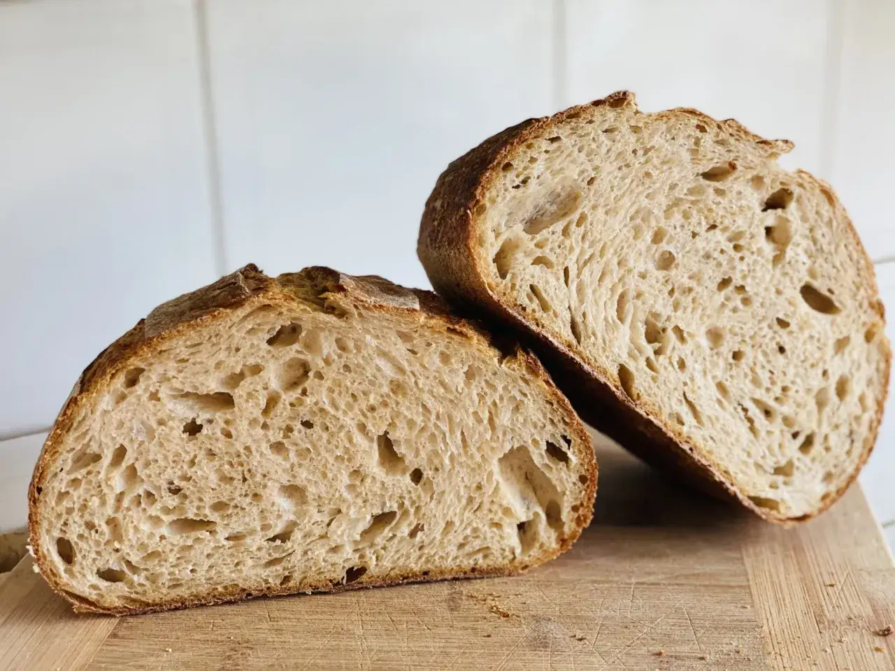 Zwei H&auml;lften eines rustikalen Sauerteigbrotes mit knuspriger Kruste und luftiger Krume liegen auf einem Holzbrett. So ist Sauerteig als Brot.