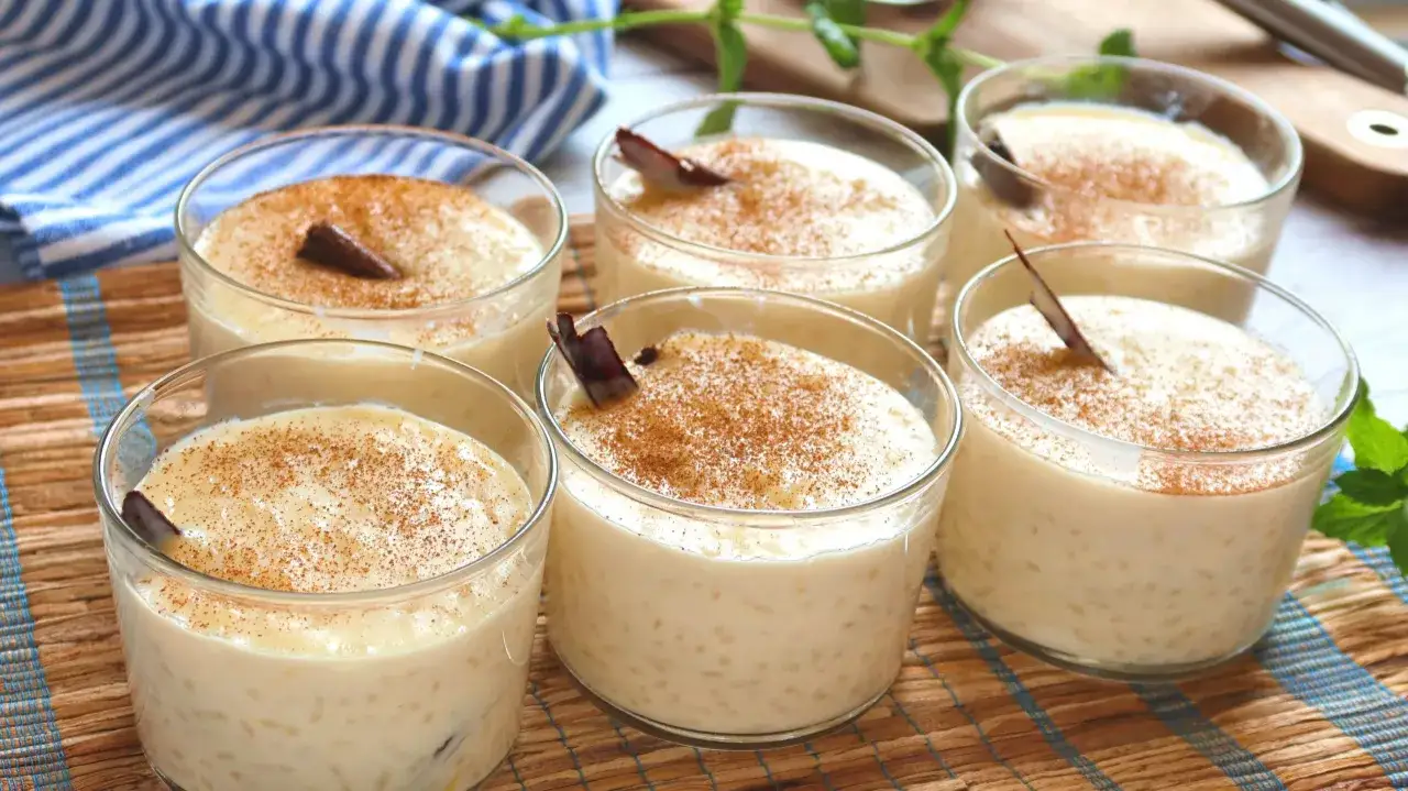 Seis vasitos de cremoso arroz con leche, espolvoreados con canela y decorados con una ramita de canela.