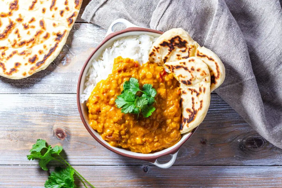 En sk&aring;l med ris och kr&auml;mig dal makhani, toppad med koriander, serveras med naanbr&ouml;d p&aring; en tr&auml;bakgrund.
