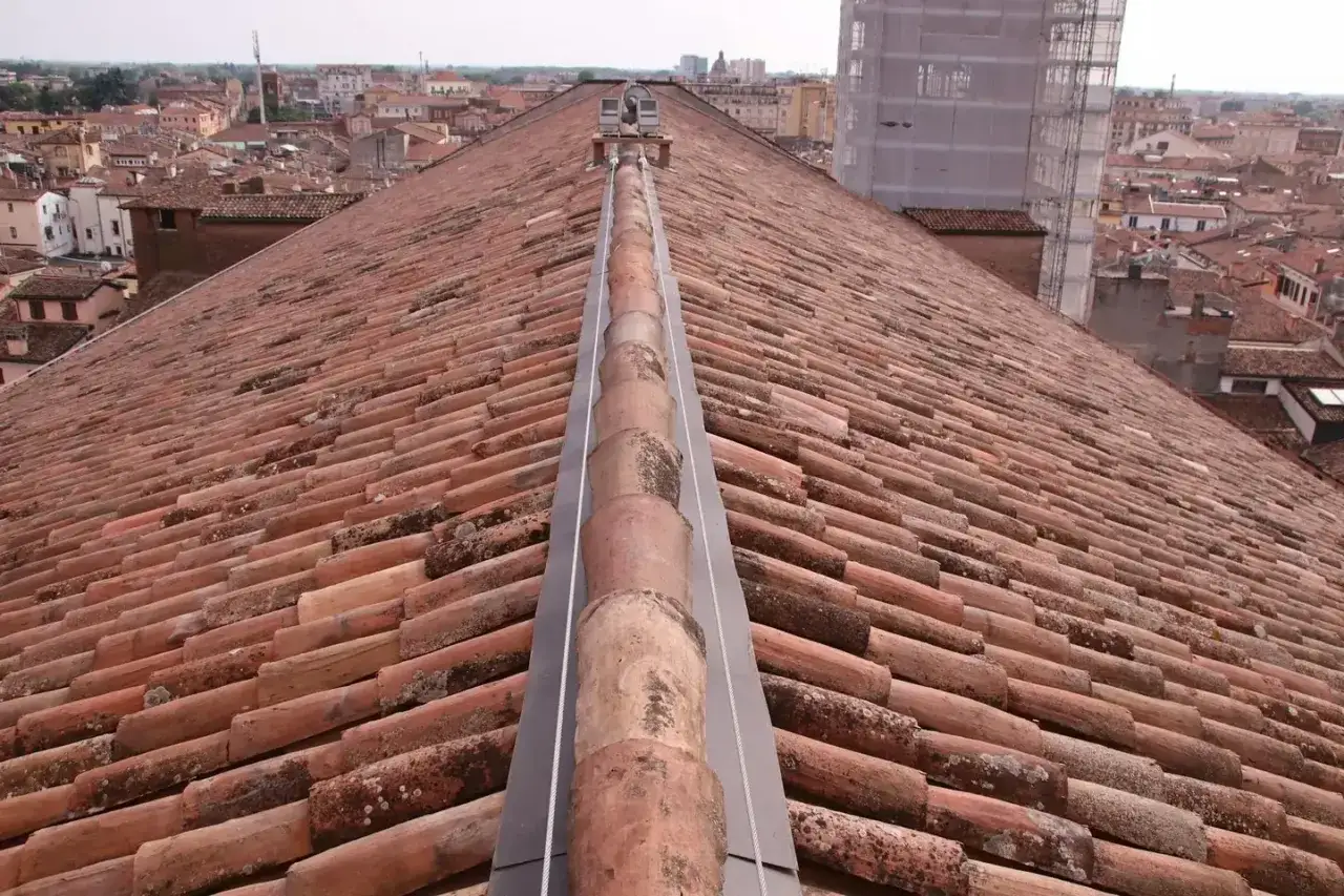 Tegole rosse antiche su un tetto inclinato, con una grondaia metallica al centro. Un esempio di come sistemare un vecchio tetto per preservare l'architettura storica.