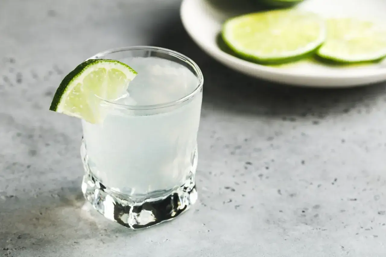 Orzeźwiający drink kamikaze, ile procent alkoholu? W szklance z plasterkiem limonki, na tle talerzyka z cytrynami.
