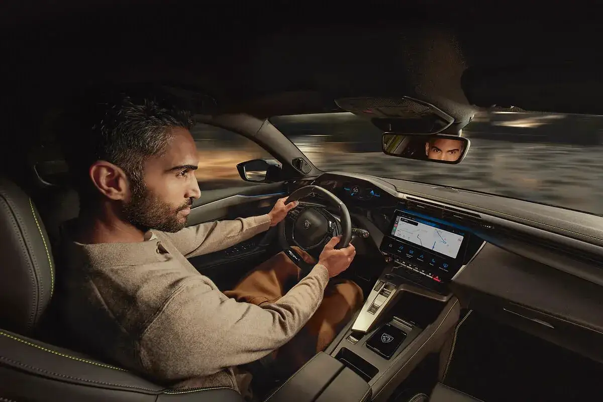 Mężczyzna prowadzi nowy Peugeot 408 nocą, zapatrzony w drogę. W lusterku wstecznym widać jego odbicie.