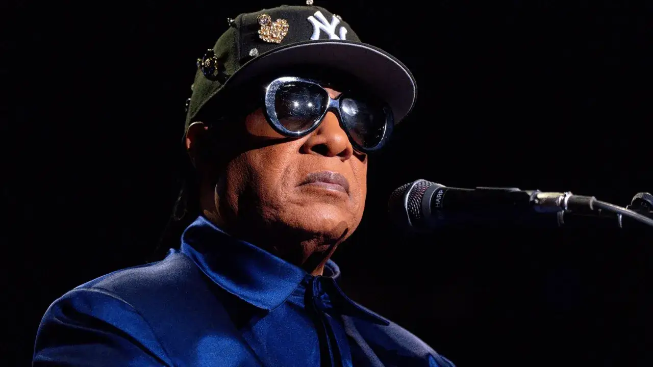 Stevie Wonder w okularach i czapce z daszkiem, gotowy do wykonania swoich niezapomnianych utworów.