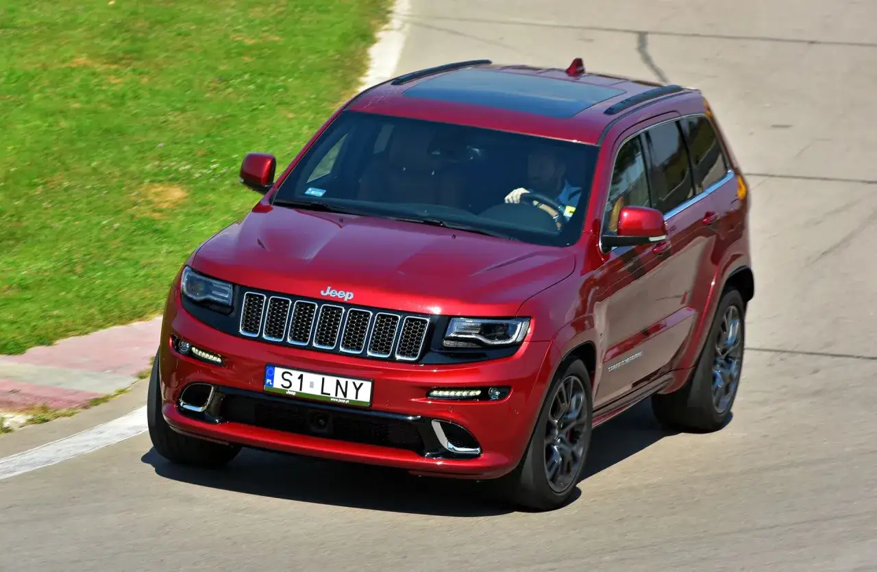 Czerwony Jeep Grand Cherokee na torze wyścigowym, z widocznymi indywidualnymi tablicami rejestracyjnymi