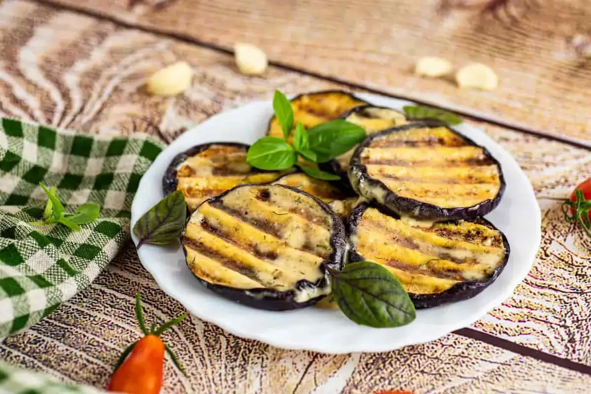 Rodajas de berenjena a la parrilla con aderezo cremoso y hojas de albahaca. ¡Perfectas para tus recetas con berenjena!