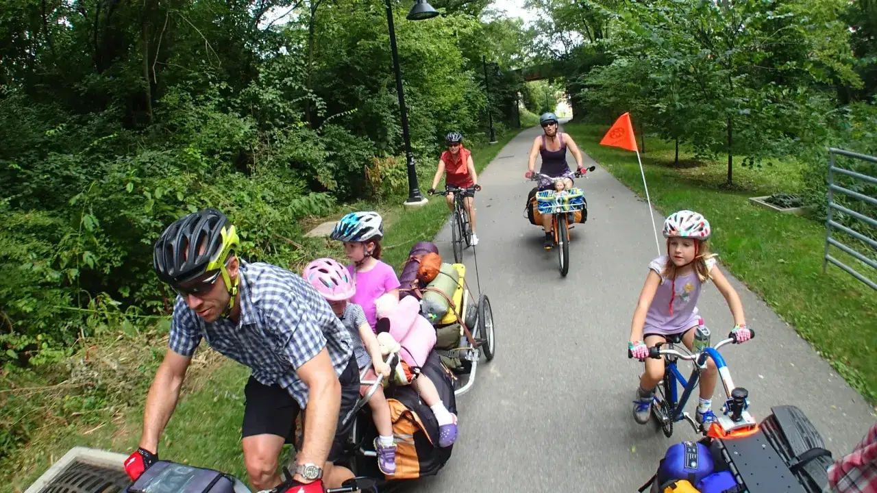 Familia disfrutando de rutas en bici con niños, pedaleando por un sendero verde con un remolque cargado.