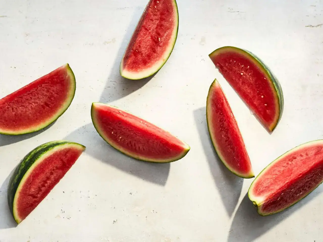 Flera saftiga vattenmelonklyftor ligger utspridda på en ljus yta. Vattenmelon nyttigt och uppfriskande!