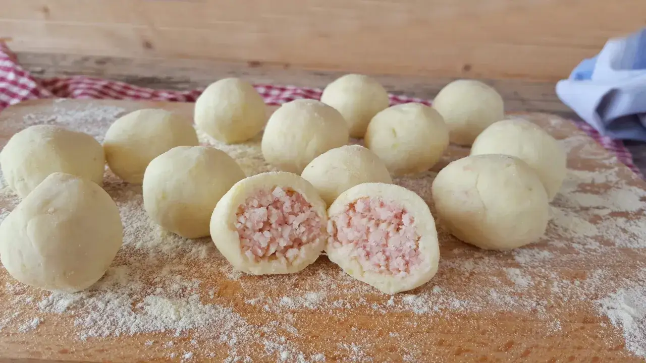 Un gruppo di gnocco di patate ripieno, uno tagliato a metà rivela un cuore saporito di carne.