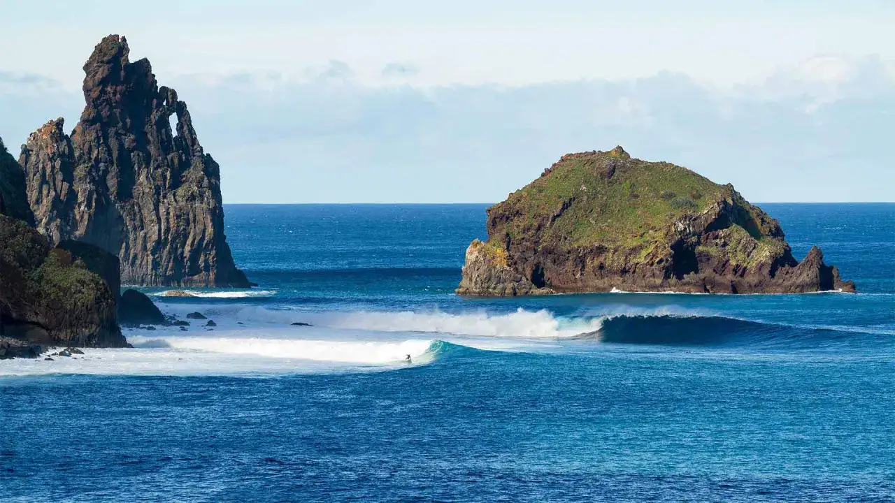 Surfer na fali przy skalistych wyspach. Piękne portugalia morze z turkusową wodą i zielonymi klifami.