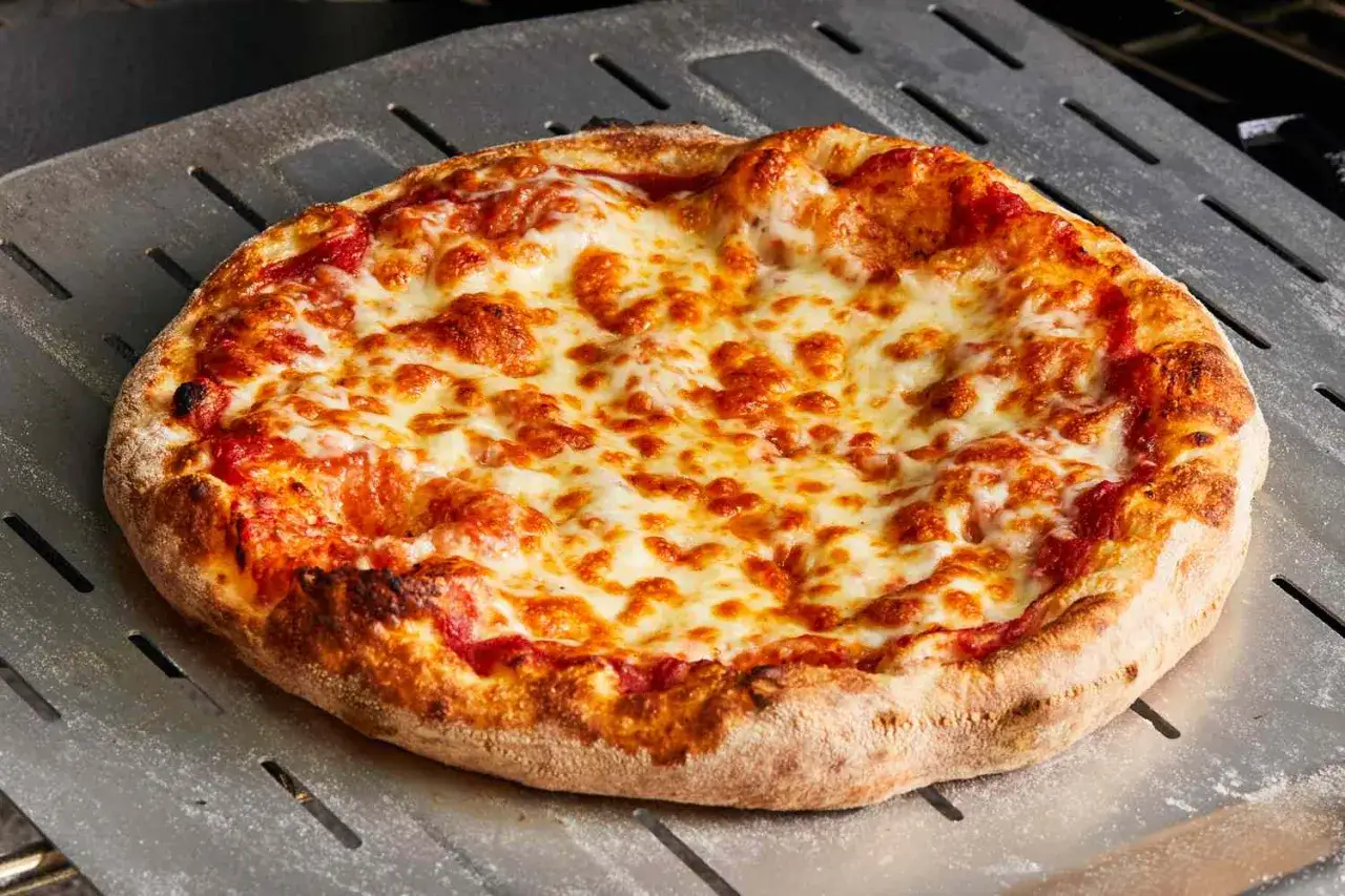 Gorąca pizza z ciągnącym się serem na łopacie. Idealny ser na pizze, kt&oacute;ry apetycznie się rozpływa.