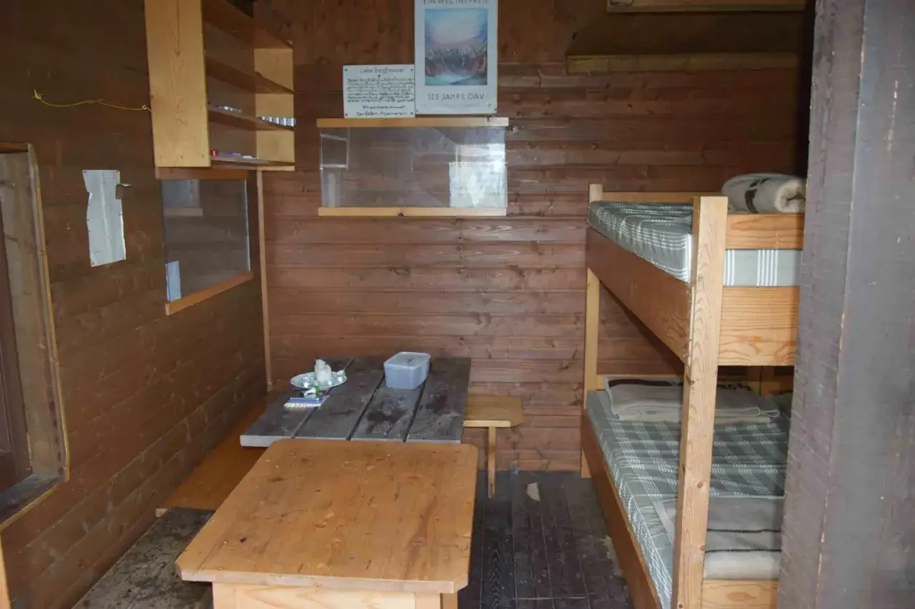 Gem&uuml;tliche biwakschachtel innen mit Holzw&auml;nden, Stockbetten und einem Tisch. Perfekt f&uuml;r eine Nacht in den Bergen.