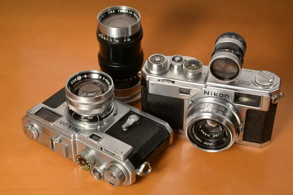 Dwa klasyczne aparaty Nikon z obiektywami, prezentujące różne nikon modele po kolei.