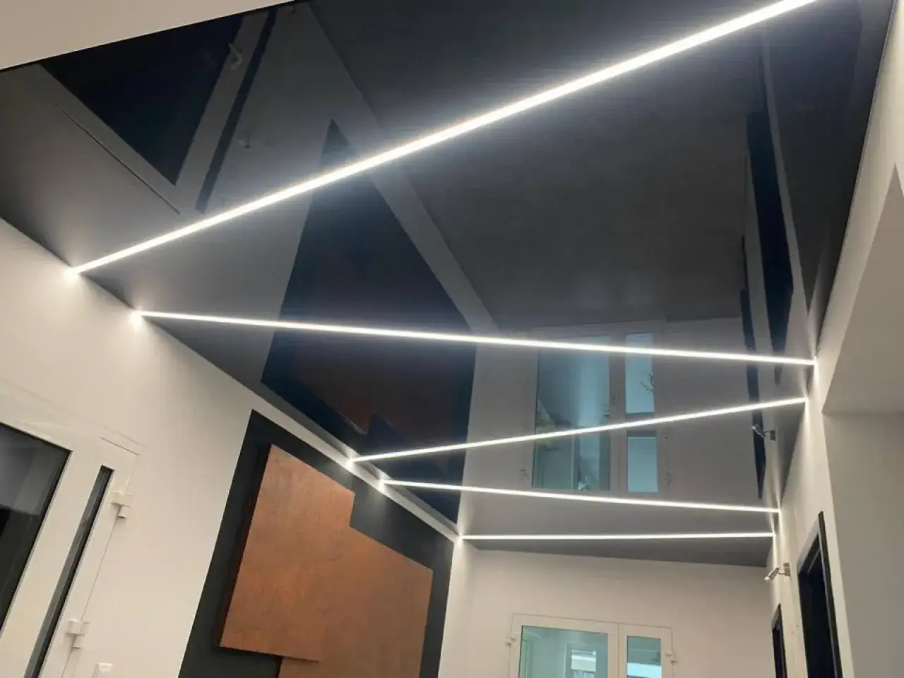 Nowoczesny sufit napinany w salonie z geometrycznymi wzorami i liniowym oświetleniem LED.