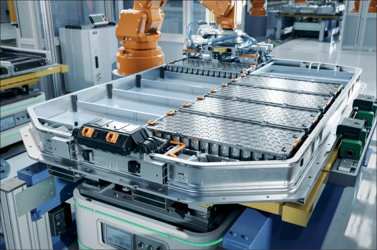 Zautomatyzowana linia produkcyjna przygotowuje moduły baterii do pojazdów elektrycznych. Robot przemysłowy montuje elementy, a w tle widać kolejne etapy procesu.