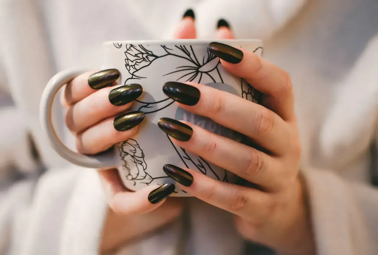 Dłonie z ciemnym, błyszczącym manicurem trzymają kubek. Czy to wady manicure japońskiego?