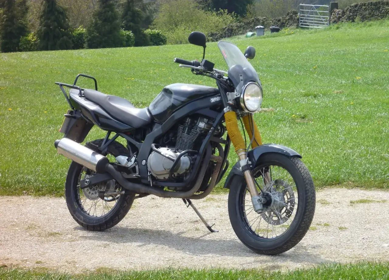 Suzuki GS 500 ficha técnica: moto negra con parabrisas, horquillas amarillas y escape cromado, aparcada en camino rural.