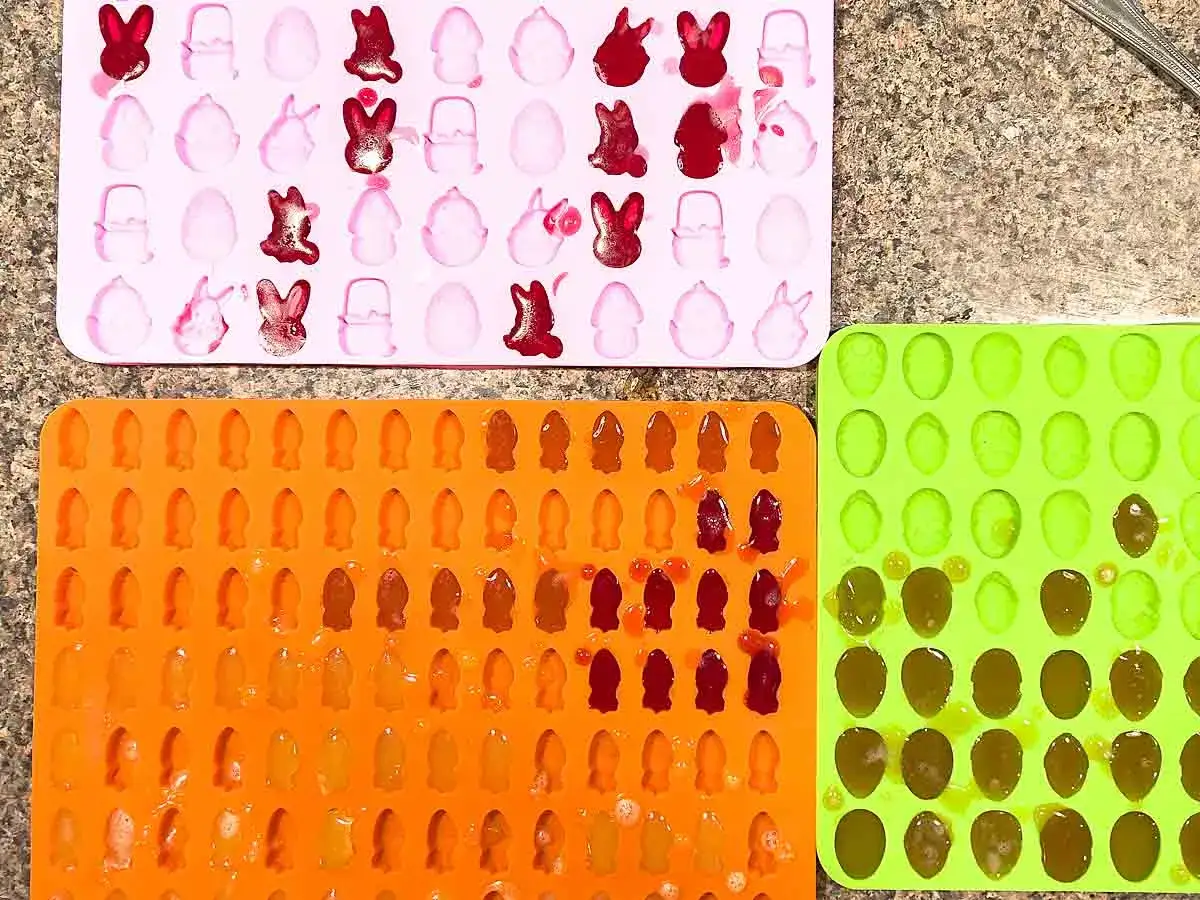 Moldes de silicona con formas de conejos y huevos, algunos ya llenos de líquido para hacer chuches.