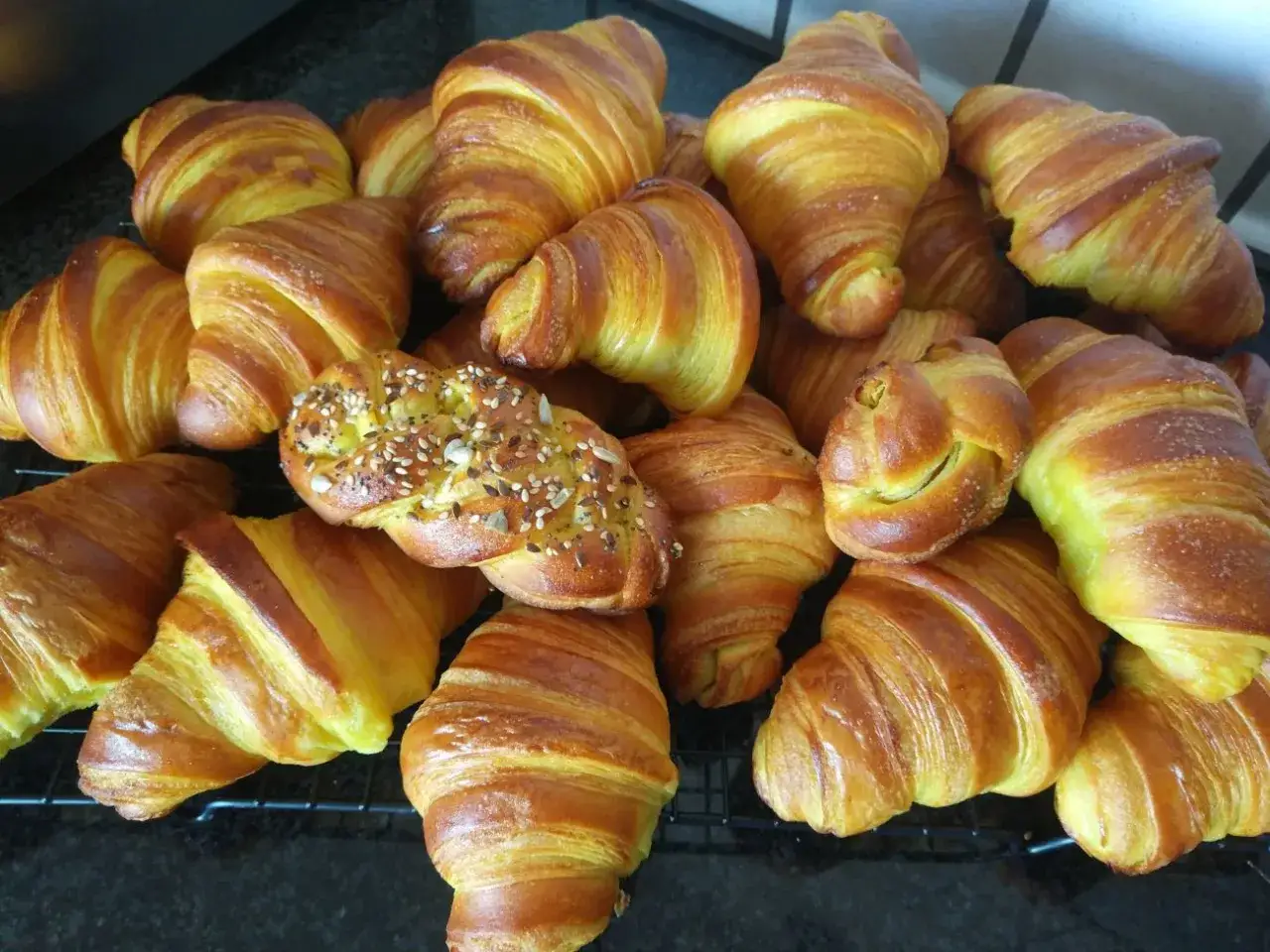 Una montagna di cornetti fatti in casa, dorati e fragranti, alcuni con semi misti, invitano a una colazione perfetta.