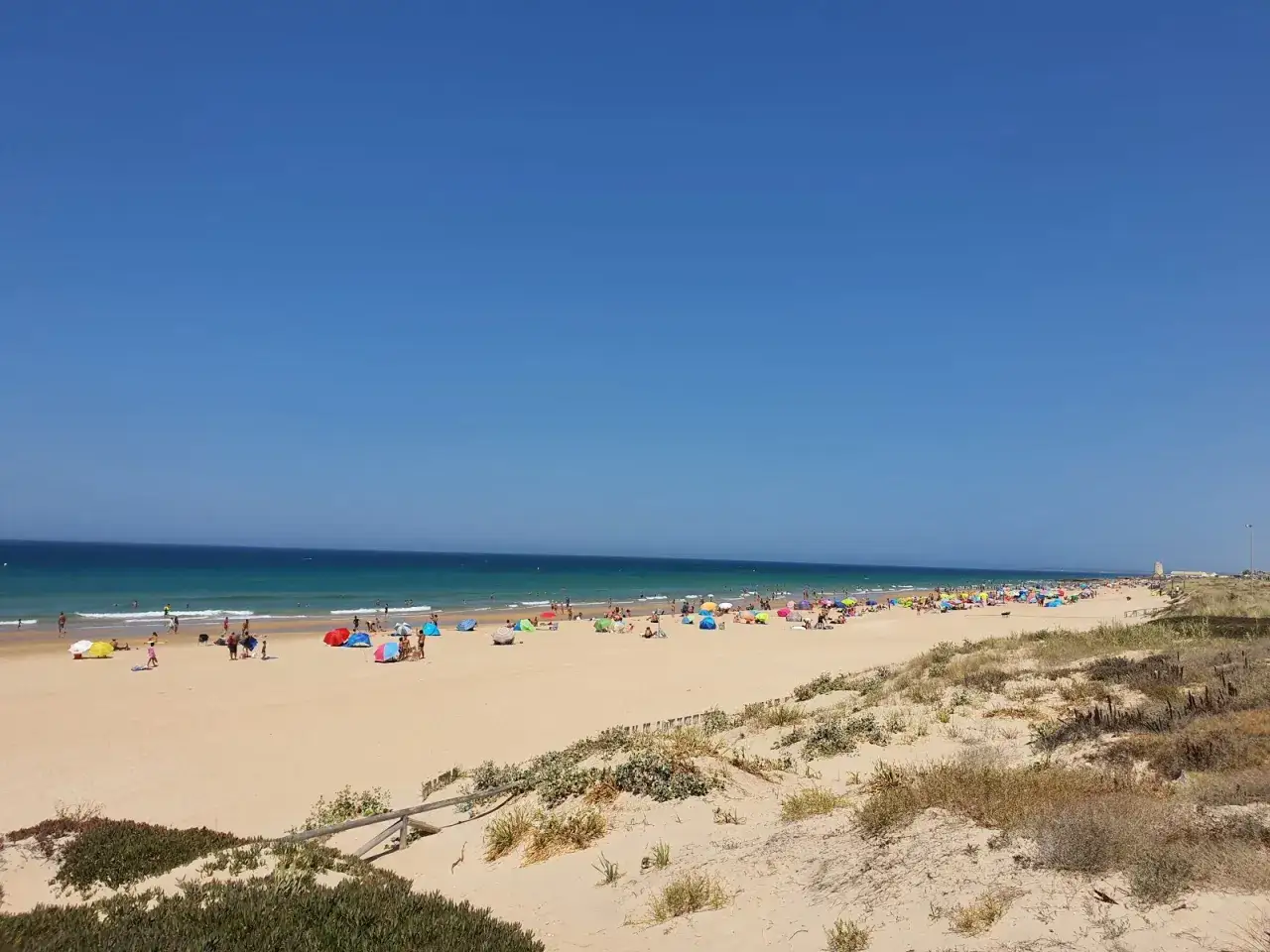 Ein sonniger Tag am Vejer de la Frontera Strand. Viele bunte Sonnenschirme und Menschen genie&szlig;en das Meer und den Sand.