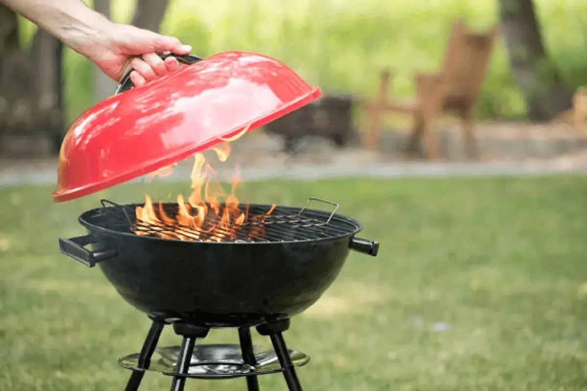 Main tenant lève le couvercle rouge d'un barbecue en feu. Il est temps de savoir comment éteindre un barbecue en toute sécurité.