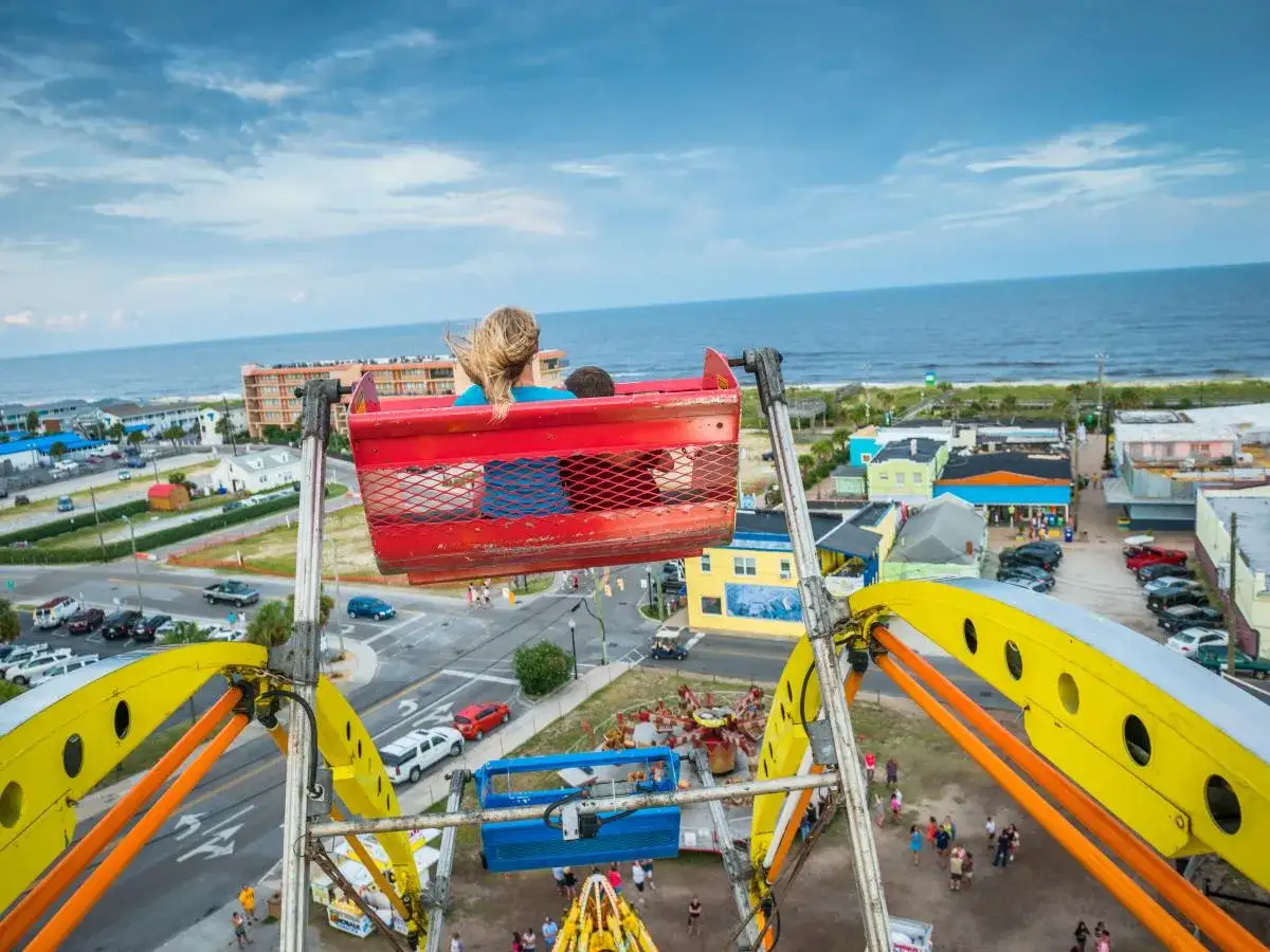 A girl enjoys a Ferris wheel ride, offering a bird's-eye view of the beach town and ocean. Fun things to do in Wrightsville Beach include amusement park rides!