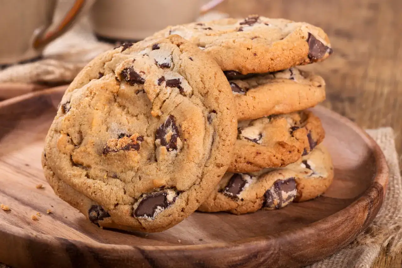 Gros plan sur un cookie aux pépites de chocolat, façon Cyril Lignac, sur une assiette en bois.