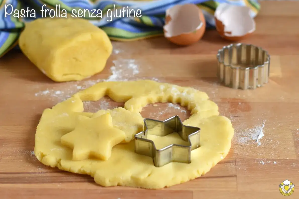 Pasta frolla senza glutine pronta per essere trasformata in biscotti a forma di stella con stampini su un tagliere di legno.