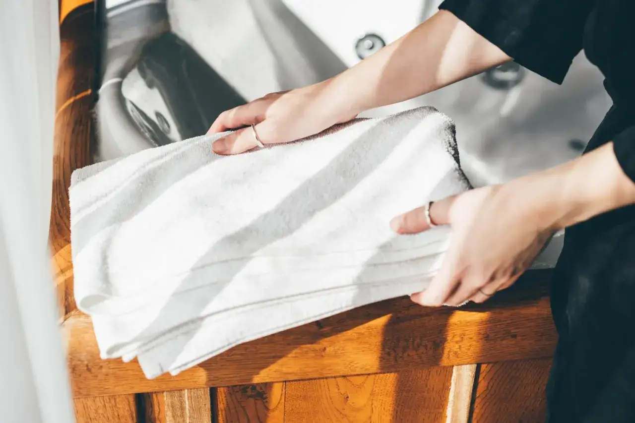 Manos sostienen toallas blancas dobladas, listas para aprender como quitar el olor a humedad de las toallas.