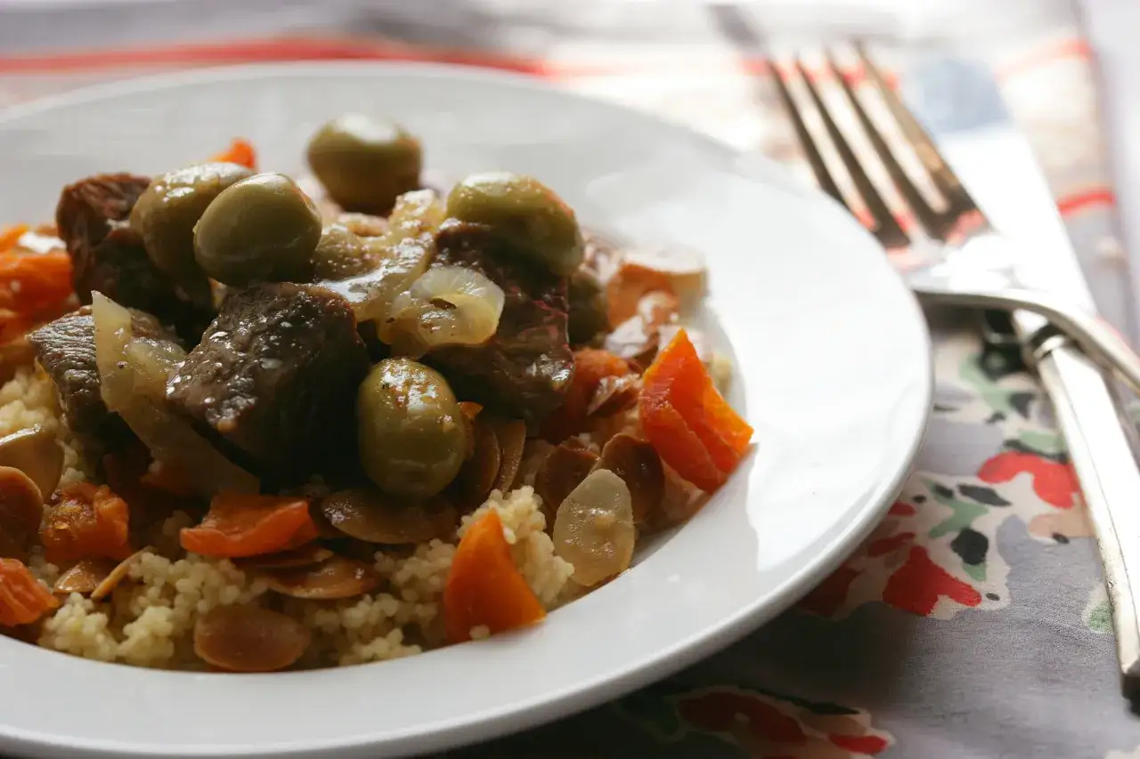 Un plat de tajine agneau savoureux avec des olives, des abricots secs et des amandes effilées sur un lit de couscous.