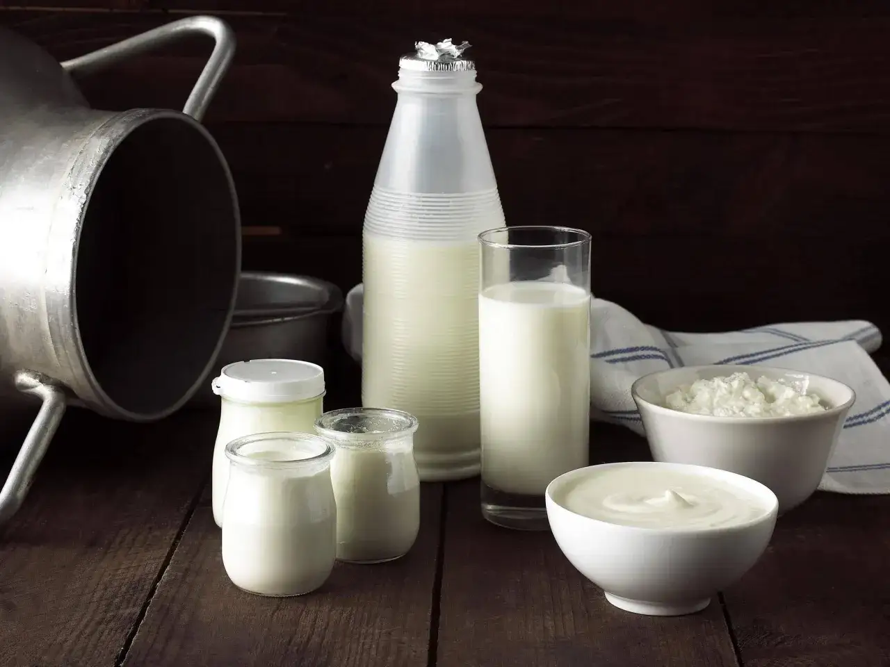 Milchprodukte auf Holztisch: Milchflasche, Joghurtgläser, Quark und eine Schüssel mit cremiger **sour cream**.