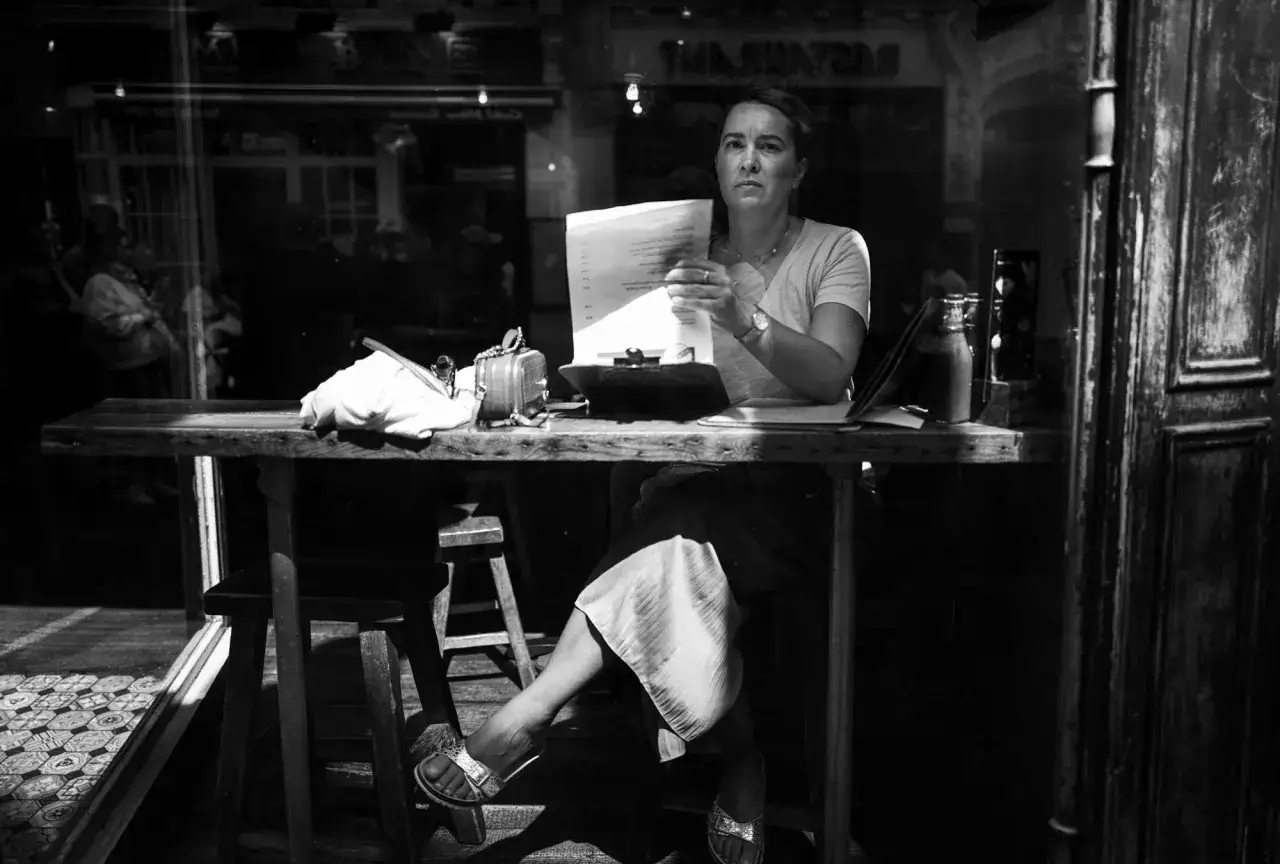 Kobieta przy stoliku w kawiarni, trzymająca dokumenty. Zdjęcie wykonane aparatem Leica Q2 Monochrom.