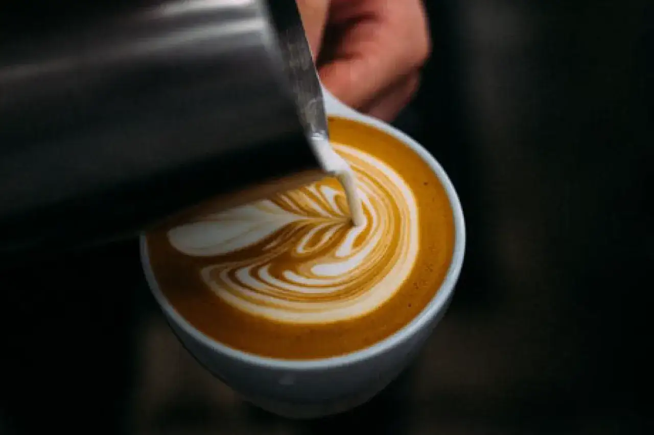 Barista tworzy latte art, wlewając mleko owsiane Inka do kawy, tworząc piękny wzór.