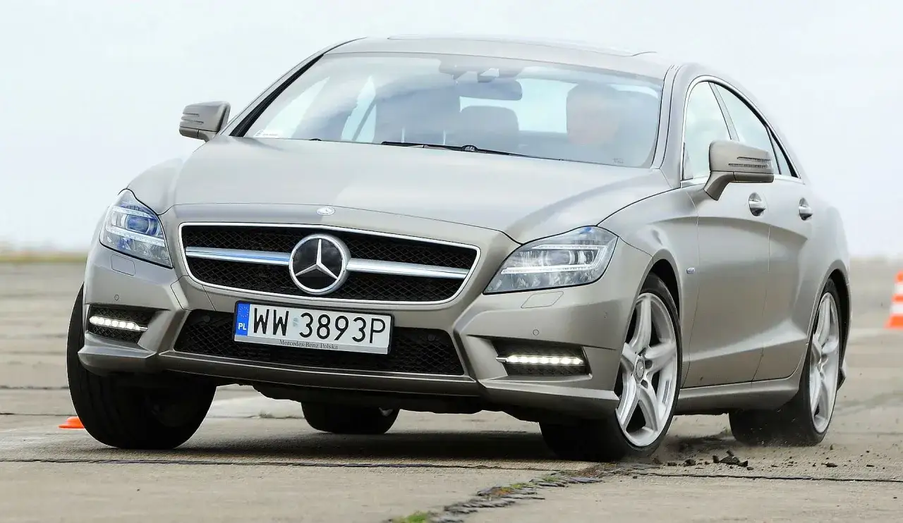 Srebrny Mercedes CLS 63 AMG Coupe na torze, z widocznym kierowcą.