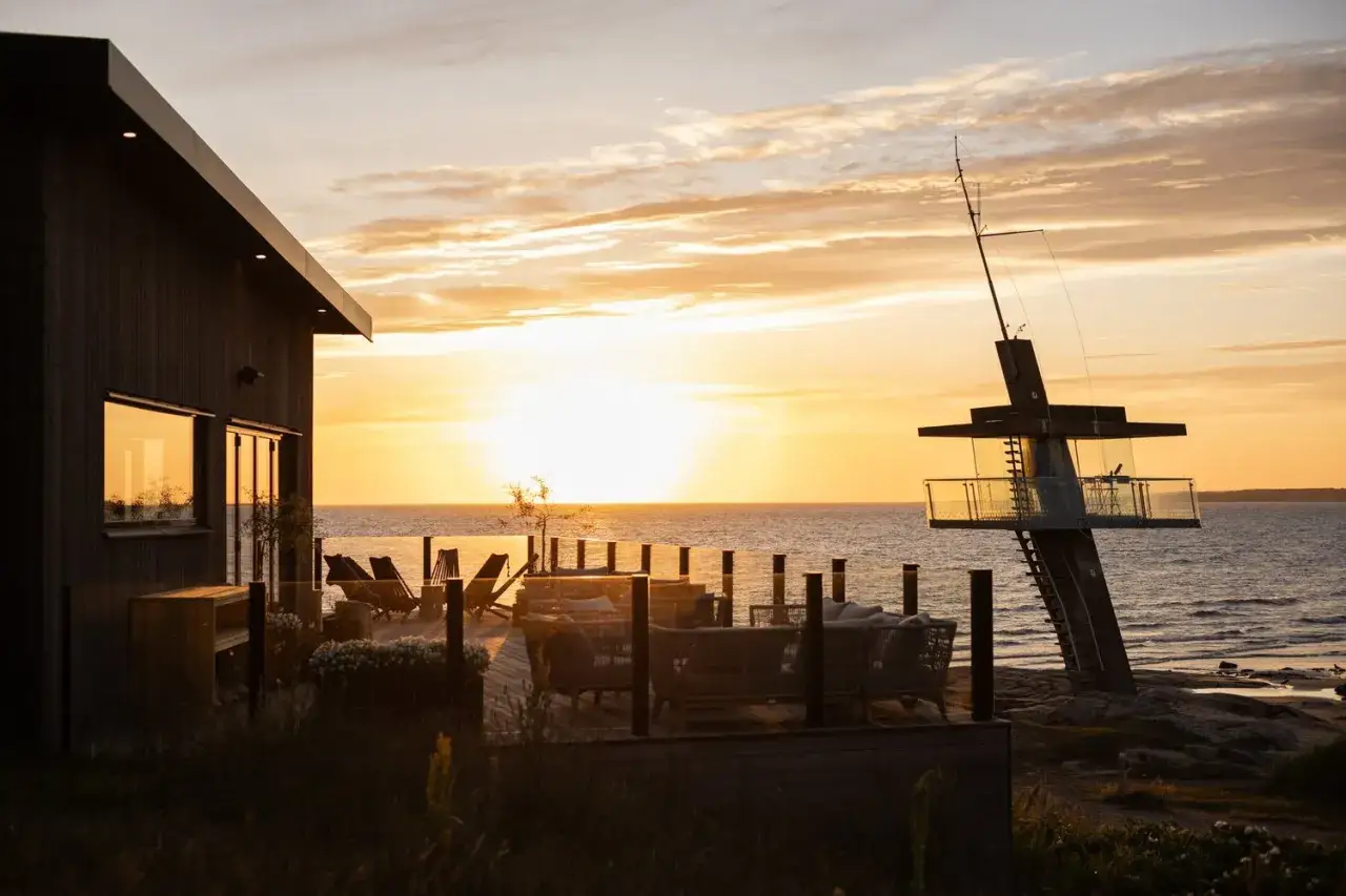Solnedg&aring;ng vid havet med en modern byggnad och utomhusm&ouml;bler. Perfekt f&ouml;r restaurangtips i Halmstad.