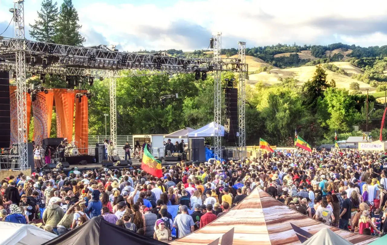 Duży festiwal muzyczny z tłumem ludzi, sceną i flagami reggae w tle.