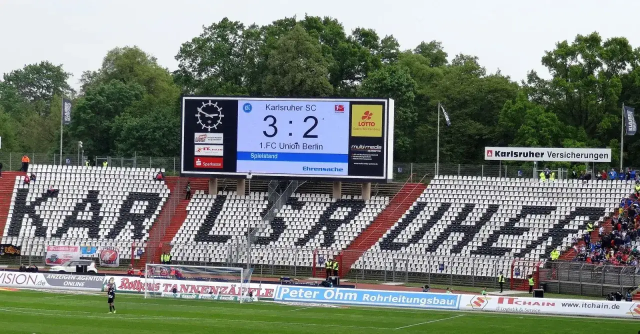 Wynik meczu Karlsruher SC 3:2 na tablicy wyników. Na trybunach widnieje napis