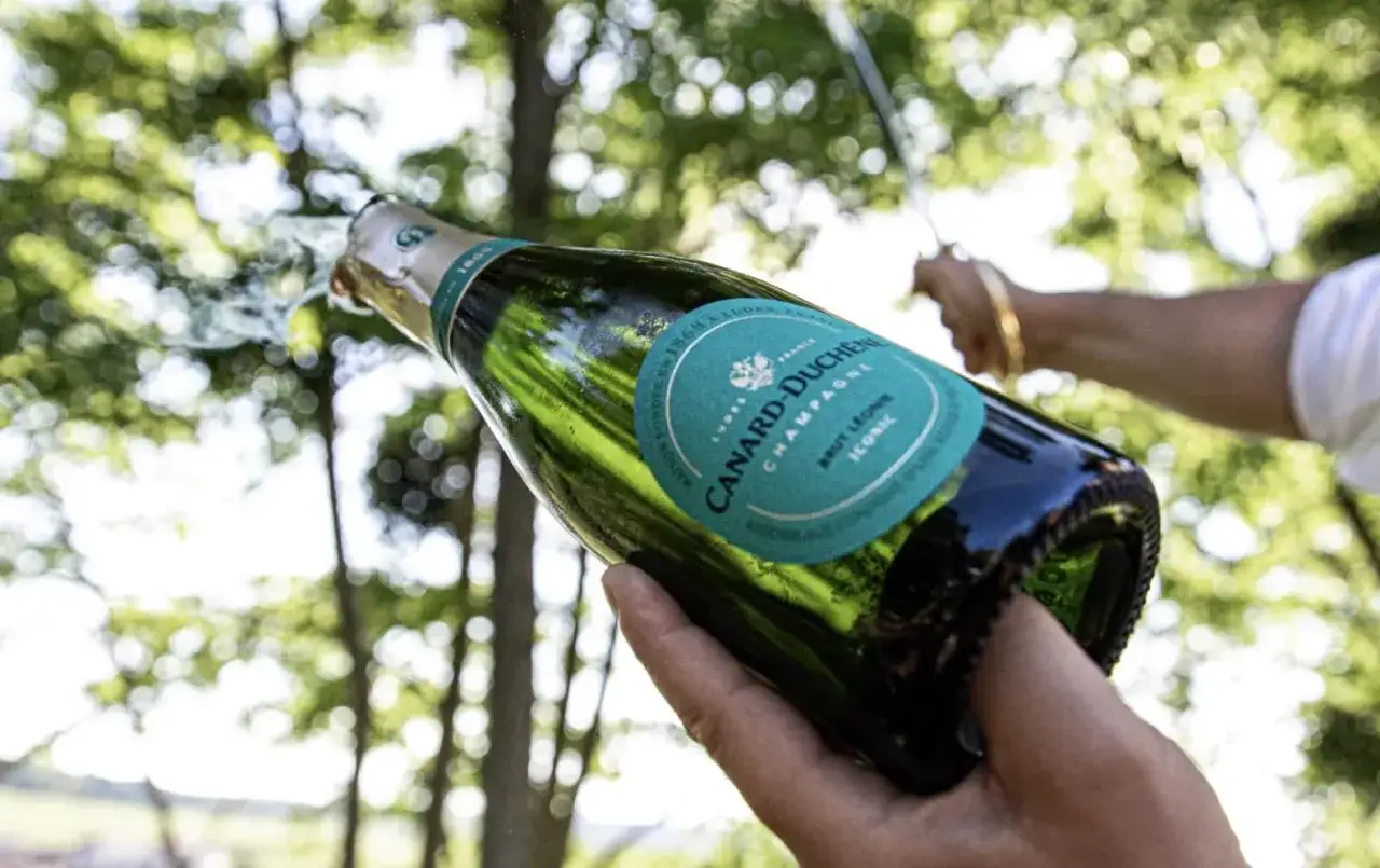 Bouteille de champagne Canard-Duch&ecirc;ne s'ouvrant, avec des bulles jaillissant. Un avis sur ce champagne iconique.
