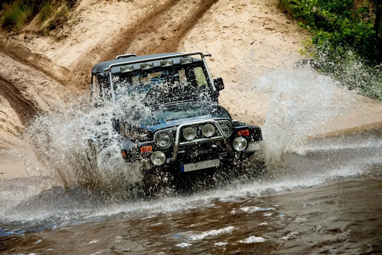 Czarny off road 4x4 zderza się z wodą, tworząc fontannę podczas jazdy po piaszczystym terenie.