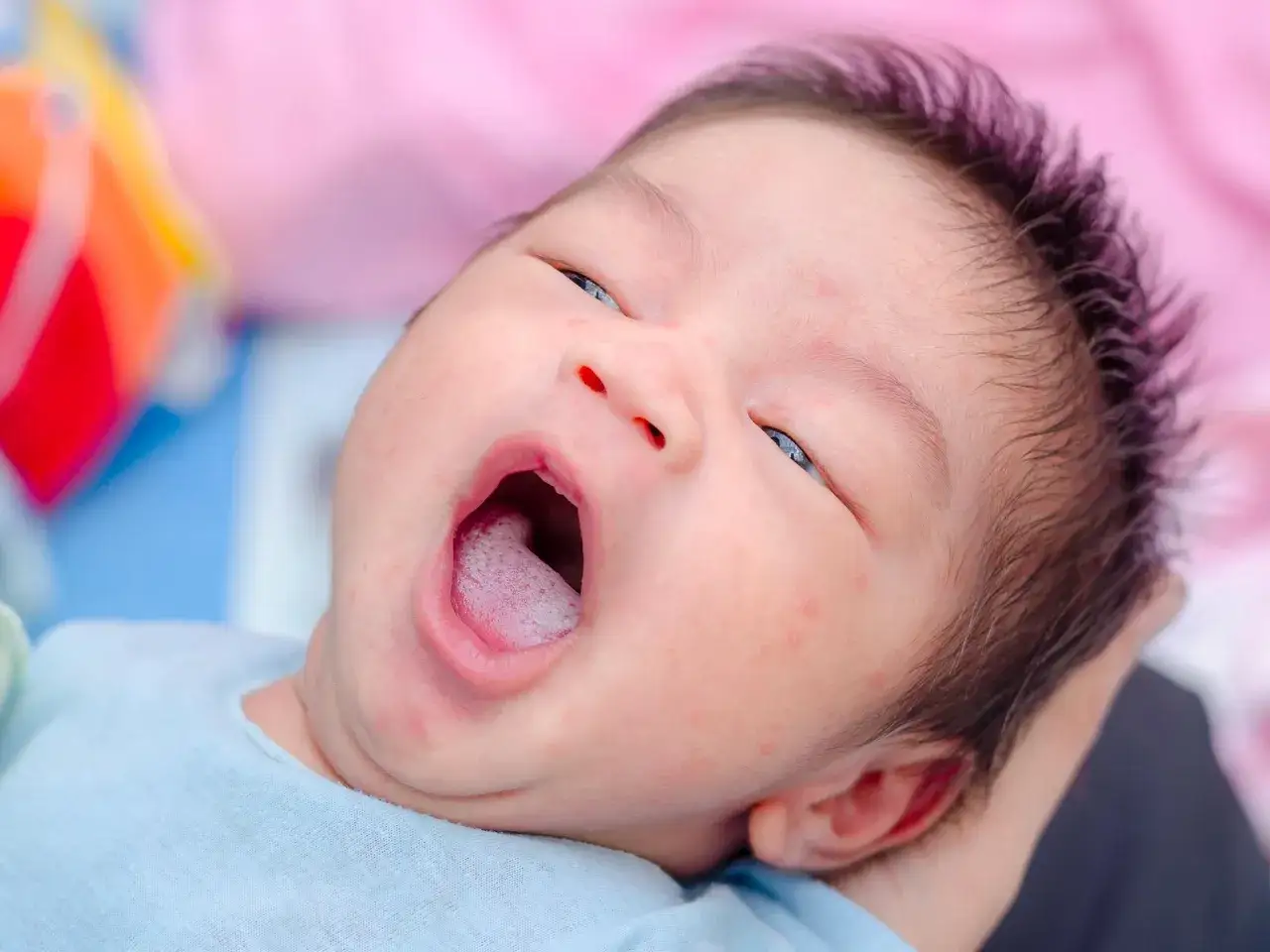 Un neonato con la bocca spalancata, come un piccolo mughetto che si apre. La sua pelle &egrave; delicata, con qualche rossore.